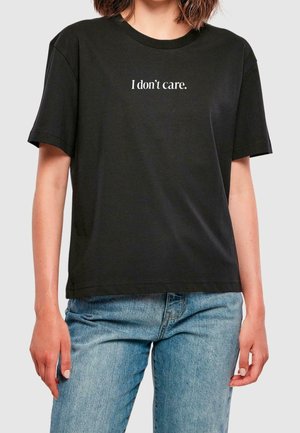 Person wearing a black t-shirt with the text "I don't care." in white, paired with light blue jeans against a plain background.