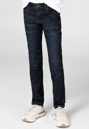 Donkerblauwe denim jeans met een slanke pasvorm, vijfzakkenontwerp en contrasterende stiksels, gecombineerd met lichtgekleurde atletieksneakers.