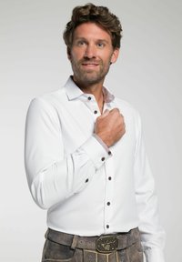 Witte lange mouwen blouse met een gedragen binnenkraag en bruine knopen, gecombineerd met grijze suède broek en een decoratieve ceintuursluiting.
