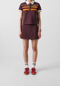 Lyhythihainen viininpunainen poolopaita keltapunahkoraidoilla, yhdistettynä samanväriseen hameeseen. Asun täydentävät punaiset lenkkarit ja raidalliset valkoiset sukat.