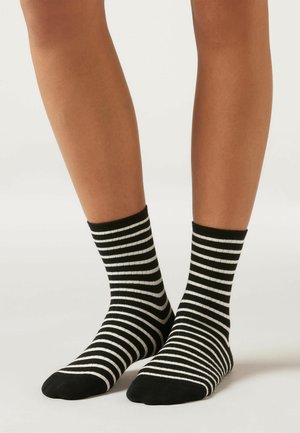 Svartvita randiga ankelsockor med ribbad textur, som har alternerande horisontella ränder och en solid svart mudd högst upp.