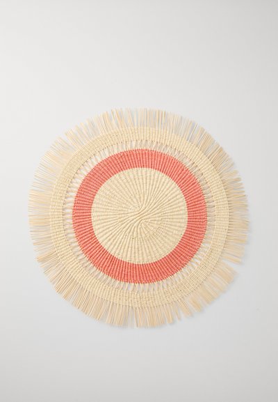 Tovaglietta rotonda intrecciata realizzata in fibre naturali di colore crema, con accenti circolari color corallo e bordi frangiati per aggiungere texture.