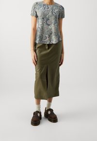 Top gris con estampado floral de manga corta, combinado con una falda verde oliva a la altura de la rodilla que presenta una abertura frontal. Calzado marrón completa el look.