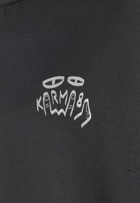 Black T-shirt featuring a silver graphic design of hands and the text "KARMA89." Material appears smooth with a breathable texture.