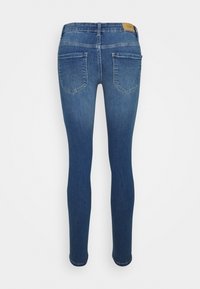 Jean skinny en denim bleu vu de dos avec deux poches et une étiquette de marque en cuir marron sur la ceinture.