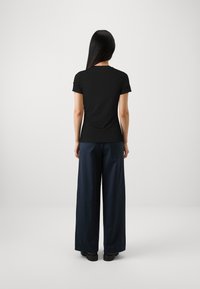T-shirt noir à manches courtes associé à un pantalon large bleu marine, présentant une texture lisse et un design minimaliste. Convient pour une tenue décontractée.