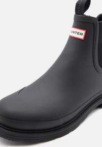 Μαύρη ελαστική μπότες μέχρι τον αστράγαλο με ελαστικές πλαϊνές πάνελ, με υφή και αντίθετο κόκκινο και λευκό λογότυπο μπροστά.