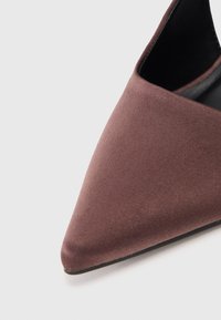 Sapatilha de bico fino em tecido castanho com uma textura suave e um interior preto ligeiramente brilhante. O salto é baixo e elegante, realçando o design streamline.