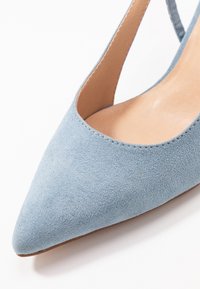 Chaussure slingback à bout pointu en daim bleu clair avec une doublure beige, sur fond blanc.