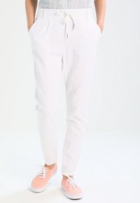 Pantalons blancs légers avec des plis, taille élastique, poches latérales et coupe fuselée. Assortis avec des baskets roses.