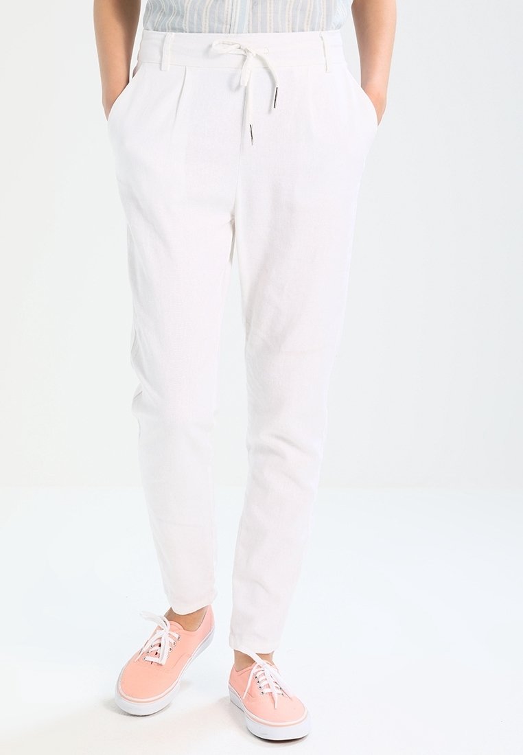 Pantalons blancs légers avec des plis, taille élastique, poches latérales et coupe fuselée. Assortis avec des baskets roses.