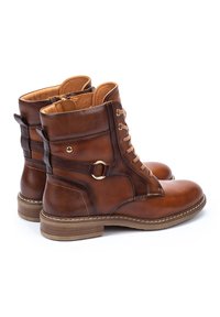 Brown leather ankle boots with a textured finish, lace-up front, side zipper, and gold-tone ring detail on the side. Rubber sole.