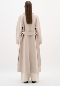 Cappotto in misto lana beige con maniche lunghe, vita con cintura e silhouette dritta. Texture liscia e lunghezza media. Nessun motivo visibile.