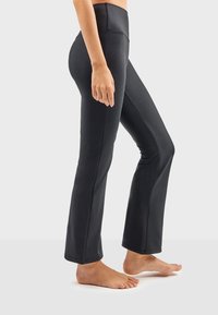 Leggings évasés noirs en tissu extensible, dotés d'une taille haute et d'une texture lisse, conçus pour le confort et la liberté de mouvement.