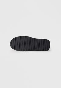 Zwarte rubberen schoenzool met gemusterde groeven voor grip, met een ronde neus en een platte vormgeving. Geribbelde oppervlakte voor extra grip.