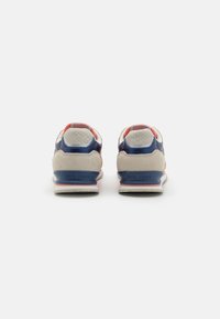 Des baskets bleu et beige avec un talon texturé, des accents rouges et une semelle blanche portant une marque sur le côté. Matériaux lisses et en suédine.