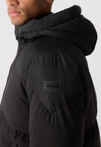 Zwarte pufferjack met capuchon, voorzien van een gequiltede textuur en een zwart Schott logo patch op de schouder.