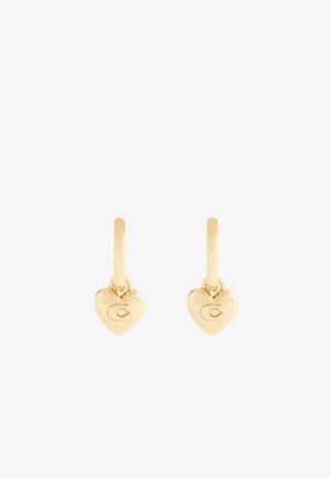 Pendientes en forma de corazón de oro con un acabado suave y un pequeño logo grabado en un lado, colgando de un aro delgado.