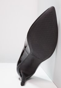 Schwarzer Lackleder-Absatzschuh mit spitzer Zehenpartie, strukturiertem schwarzem Gummisohle und einem stabilen, niedrigen Absatz. Markenlogo auf der Sohle sichtbar.