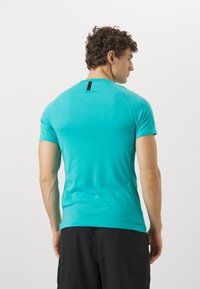 Türkisfarbenes Sport-T-Shirt mit kurzen Ärmeln, Rundhalsausschnitt und strukturierten Seiteneinsätzen, mit einem schwarzen Akzent am hinteren Halsausschnitt.