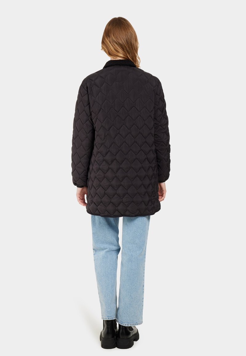 Schwarze gesteppte Jacke mit Rautenmuster, mit Kragen, langen Ärmeln und mittellangem Schnitt. Getragen über hellblauen geraden Jeans.