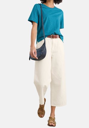 Personne portant une chemise à manches courtes bleu sarcelle, un pantalon large couleur crème avec ceinture marron, des sandales marron à lanières et un sac bandoulière bleu à motifs.