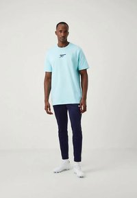 T-shirt en coton bleu clair à manches courtes, avec un petit logo marine sur la poitrine, associé à un pantalon slim fit marine foncé et des chaussures blanches.