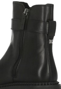 Stivaletto alla caviglia in pelle nera con chiusura a cerniera laterale, dettagli cuciti e cinturino decorativo. La suola presenta piccoli borchietti lungo il bordo.