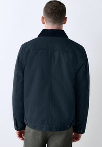 Chaqueta azul oscura con cuello de pana y cierre de botones a presión. Presenta costuras limpias y un diseño de corte recto, fabricada con un tejido resistente.