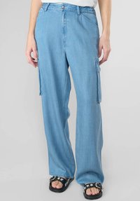 Pantaloni cargo azzurri realizzati in denim, con gambe larghe, tasche laterali e zip. Abbinati a sandali neri.