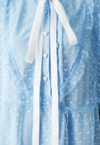 Ljusblått genomskinligt klänning med hjärt-mönster, volangkanter och vita satinhalsband. Har hjärtformade knappar längs fram.