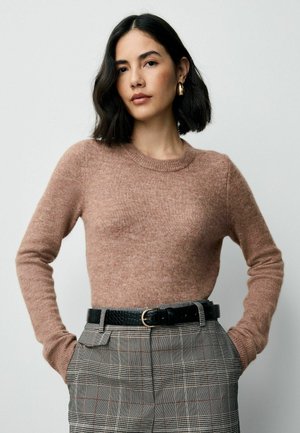 Hellbrauner, gestrickter Pullover mit langen Ärmeln und Rundhalsausschnitt, kombiniert mit karierter Hose und einem schwarzen Gürtel. Angenehme Textur.