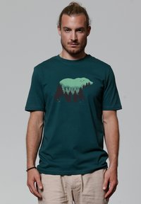 Teal katoen t-shirt met een silhouet van een beer en een bosontwerp in groen en zwart. Ronde halslijn en korte mouwen.