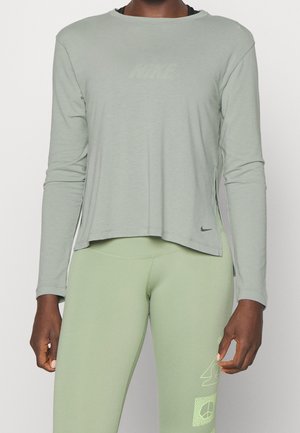 Persona con camiseta de manga larga Nike de color verde claro y leggings verdes a juego con logotipos mínimos e impresiones gráficas en el muslo izquierdo.