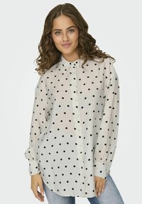 Witte blouse met zwarte stippen, lange mouwen en een kraag; lichtgewicht stof met een iets losvallende pasvorm.