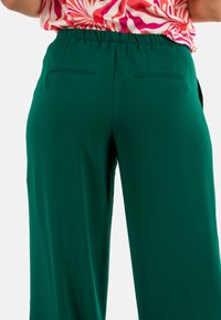 Pantaloni ampi verdi con vita elastica, dotati di due tasche posteriori e un tessuto liscio e leggero.