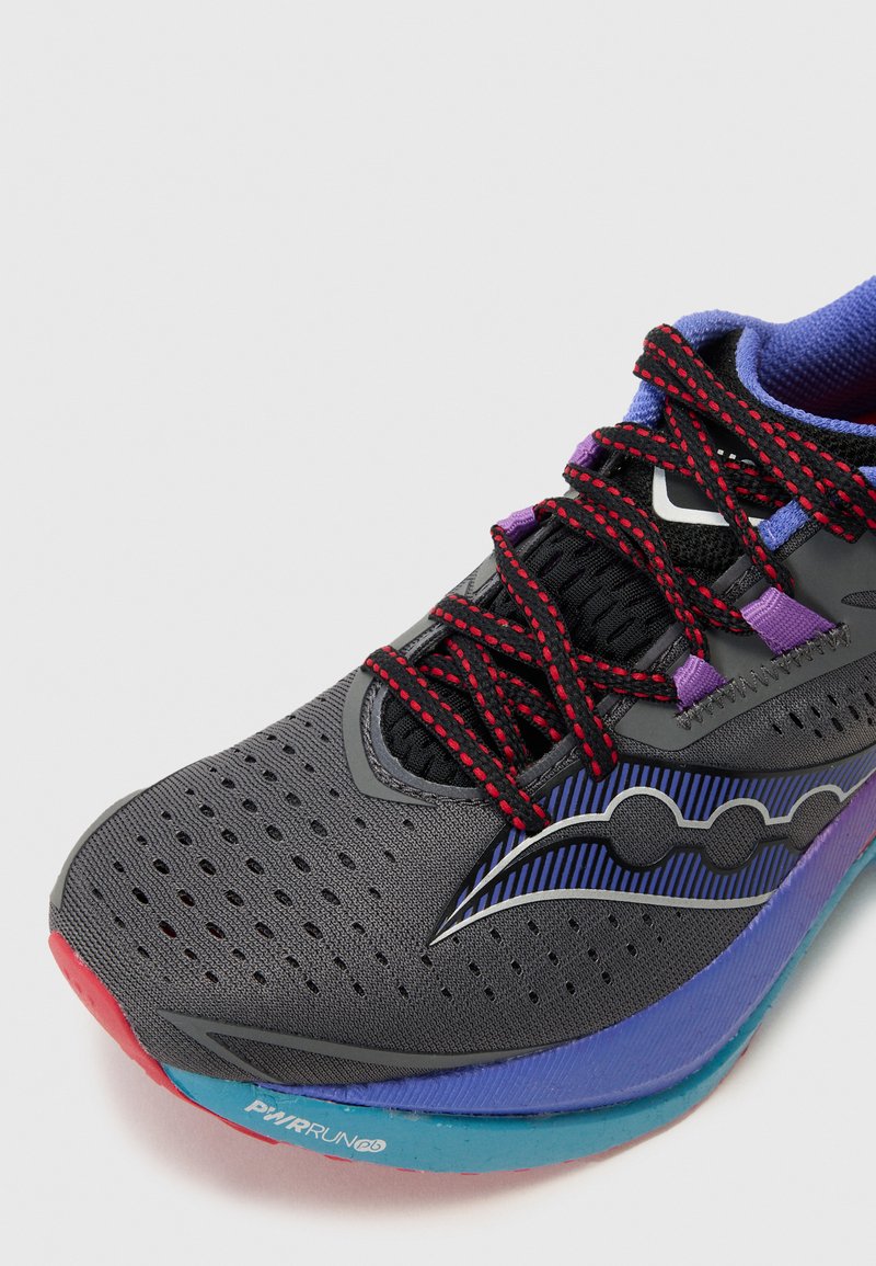 Zapatilla deportiva gris con parte superior de malla, acentos rojos, cordones negros y una mediasuela con degradado púrpura. Presenta orificios de ventilación y un diseño con patrones.