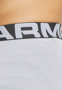 Witte stof met een gestructureerd oppervlak, met een zwarte elastische tailleband met "ARMOUR" in grote witte letters.