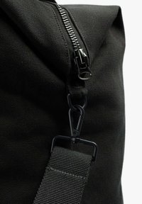 Bolso de lona negro con cierre de cremallera, superficie texturizada y una correa gris con un resistente clip de sujeción.