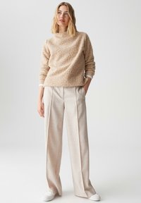 Beige textuurtrui met een hoge halslijn, gecombineerd met lichtbeige wijde broekspijpen en witte sneakers. De trui heeft ribgebreide boorden.