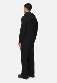 Giacca a maglia nera con cappuccio e pantaloni larghi coordinati, caratterizzati da una texture soffice e una vestibilità rilassata. Indossata con sneakers.