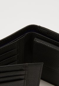 Cartera de cuero negro con acabado texturizado, que cuenta con múltiples ranuras para tarjetas y una sección con cremallera para monedas, parcialmente abierta.
