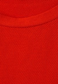 Roter Strickstoff mit einer strukturierten Oberfläche. Der Stoff hat einen gerippten Halsausschnitt, der die leuchtende Farbe und die weiche Textur betont.