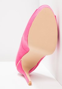 Růžová semišová lodička na vysokém podpatku s špičatou špičkou a tenkým stiletto. Texturovaná podrážka s vertikálními pruhy. Boční pohled na bílém pozadí.