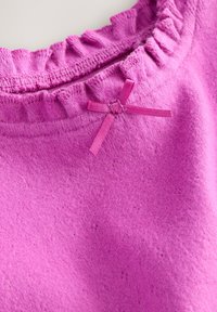 Prenda de punto rosa con un escote fruncido y un pequeño lazo rosa como detalle. La textura es suave y ligeramente aterciopelada.