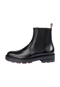 Stivale alla caviglia in pelle nera con pannelli elastici laterali e accenti perforati. Suola chunky con dettagli rossi sul tallone. Design classico alla Chelsea.