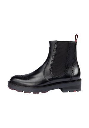 Stivale alla caviglia in pelle nera con pannelli elastici laterali e accenti perforati. Suola chunky con dettagli rossi sul tallone. Design classico alla Chelsea.