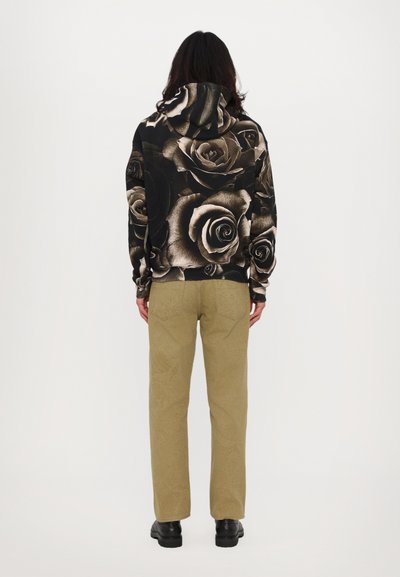 Hoodie med svart och beige ros-mönster, matchad med khakifärgade texturerade byxor. Skorna är svarta stövlar. Utsikten är från baksidan.