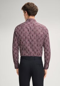 Langärmliges Hemd aus bordeauxfarbenem Stoff mit einem detaillierten weißen Blumenmuster, kombiniert mit schwarzen Hosen, die ein strukturiertes Rückendesign zeigen.