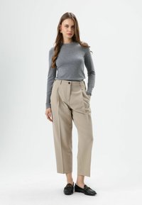 Gray long-sleeve top paired with high-waisted, beige wide-leg trousers. Model wears black loafers and stands on a plain background.